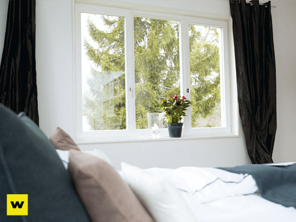 Helles Schlafzimmer mit großem Fenster, Vorhängen und Topfpflanze auf der Fensterbank.