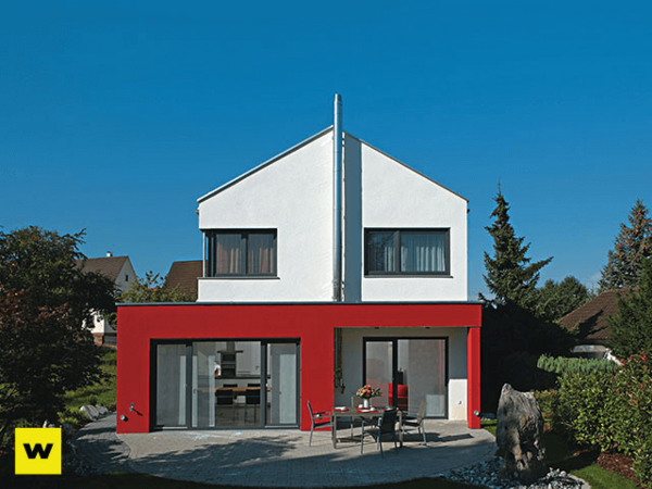 Modernes Einfamilienhaus mit roter Fassade und großer Terrasse im Garten bei Sonnenschein.