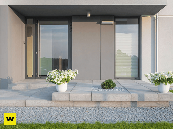 Moderner Hauseingang mit großen Fenstern, Steinfliesen und Blumenkübeln auf der Terrasse.