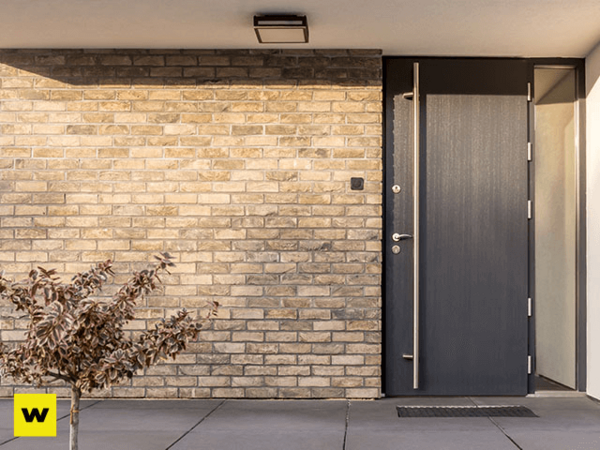 Moderne Haustür aus Aluminium vor heller Klinkerfassade mit kleiner Pflanze im Eingangsbereich.